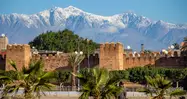 Murallas de la ciudad de Taroudant con palmeras en primer plano y los picos nevados del Atlas al fondo.