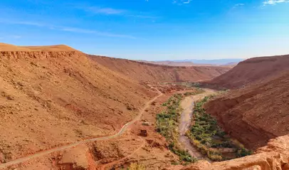 Vista panorámica de las carreteras serpenteantes del Alto Atlas entre colinas áridas y un río rodeado de vegetación