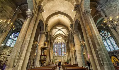 Interior gótico de la Basílica de San Nazario en Carcasona, con vitrales, columnas y bancos de madera.