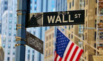 Señal de Wall Street y Broad Street con banderas estadounidenses y edificios del distrito financiero de Nueva York.