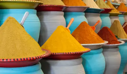 Montículos de especias tradicionales marroquíes en tonos cálidos, dispuestos en mercados locales sobre recipientes de cerámica.