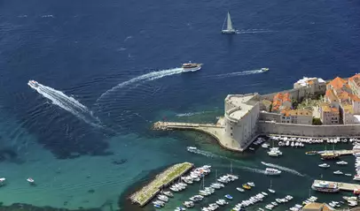 Vista aérea del puerto de Dubrovnik con barcos y fortificación redonda al borde del mar.