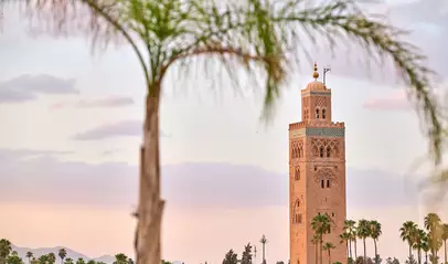 Minarete de la mezquita Koutoubia de Marrakech enmarcado por palmeras al atardecer, símbolo de la ciudad.