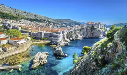 Murallas de Dubrovnik bordeando la costa, acantilados y aguas turquesas desde un punto elevado.