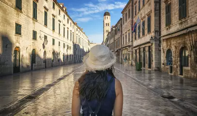 Mujer con sombrero paseando por la calle Stradun de Dubrovnik, al fondo la torre del reloj del casco antiguo.