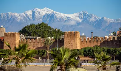 Murallas de la ciudad de Taroudant con palmeras en primer plano y los picos nevados del Atlas al fondo.